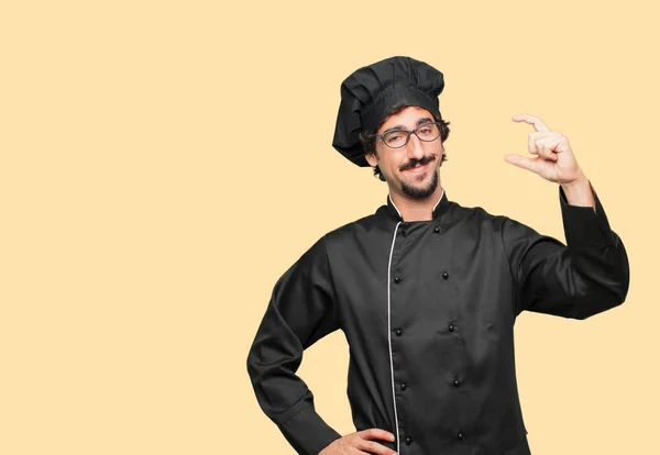 young crazy man as a chef smiling with a satisfied expression showing a small object or concept, holding it with single hand.