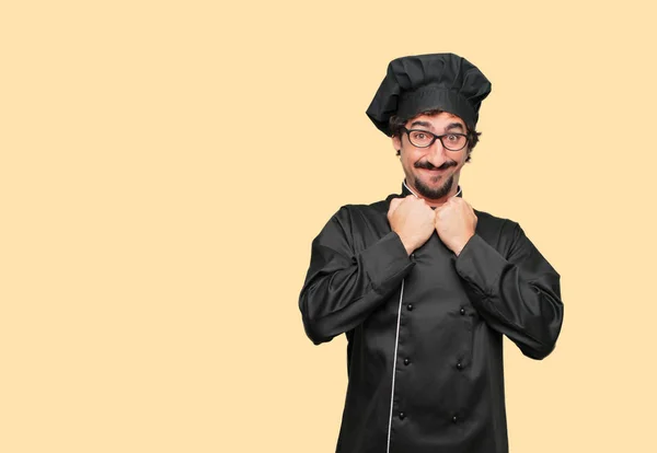 young crazy man as a chef with a happy surprised expression, eyes wide open and broad smile, with both hands clenched under chin showing shock.