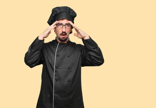 young crazy man as a chef with a surprised, amazed expression, holding both hands to forehead and mouth wide open in shock.