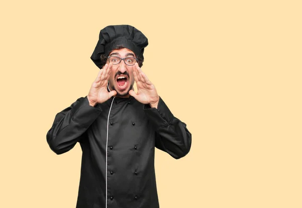 young crazy man as a chef shouting loud like crazy, calling with hand with an angry expression, communicating a big announcement.
