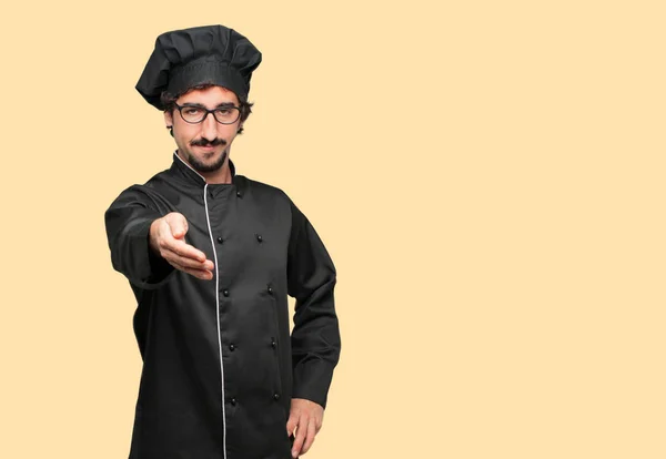 young crazy man as a chef with a serious, confident, proud and stern expression offering a handshake, closing a deal, or greeting and welcoming you.
