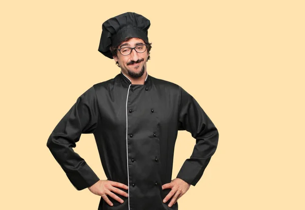 young crazy man as a chef smiling proudly and confidently with arms hands on hips in akimbo pose, happy and sure of success, giving an \