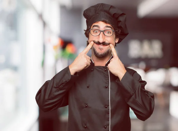 young crazy man as a chef forcing a smile on face with both index fingers, as if sending a \