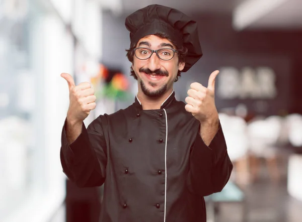 young crazy man as a chef with a satisfied, proud and happy look with thumbs up, signaling OK with both hands, sending a positive, 