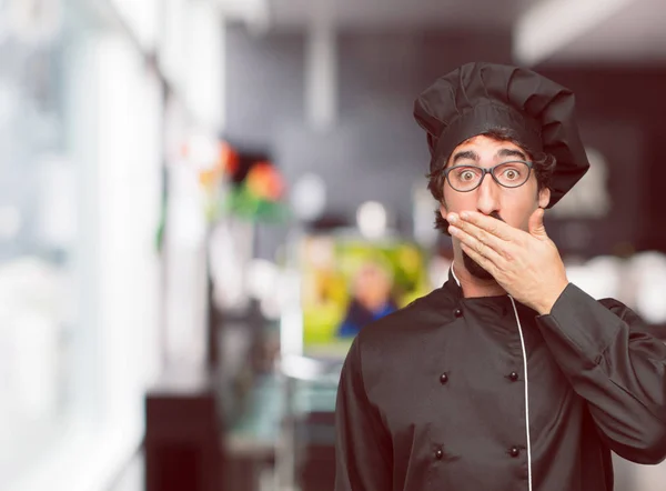 young crazy man as a chef Covering mouth with hand with a gesture of surprise, in order to remain silent and keep a secret.