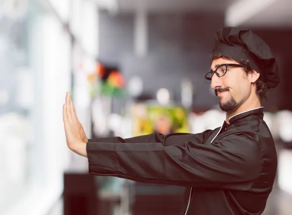 young crazy man as a chef signaling stop with both palms of hands facing forward, with a serious and stern expression, forbidding. Mid-lateral view.