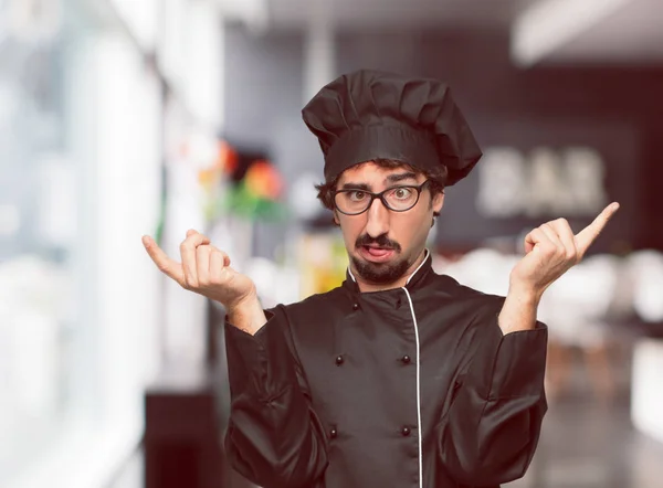 young crazy man as a chef shouting with a crazy, amazed look of surprise, with both hands in the air.