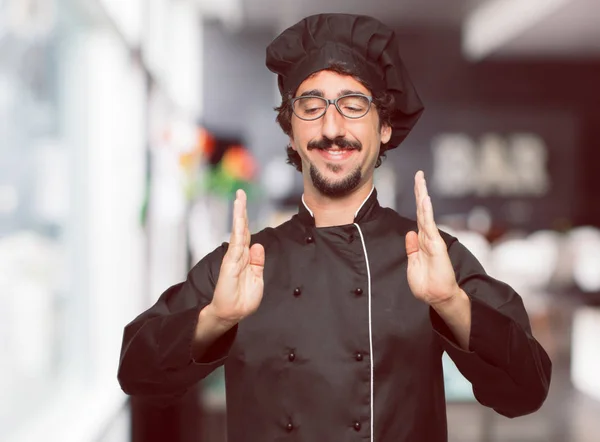 年轻的疯狂的人作为厨师微笑着一个满意的表达 显示一个对象或概念 这是在双手之间 在前面 — 图库照片