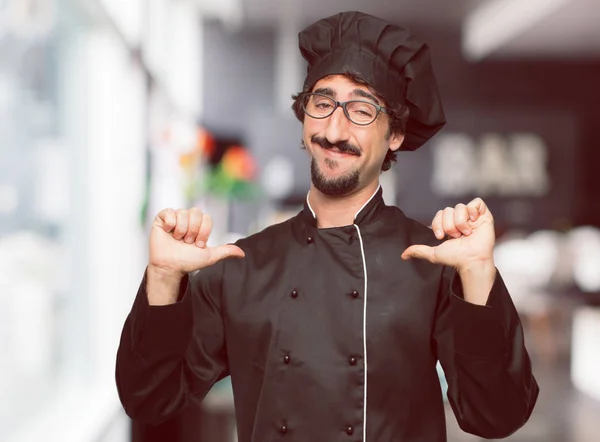 young crazy man as a chef with a proud, happy and confident expression; smiling and sure of success, pointing to one's self with both hands, giving an 