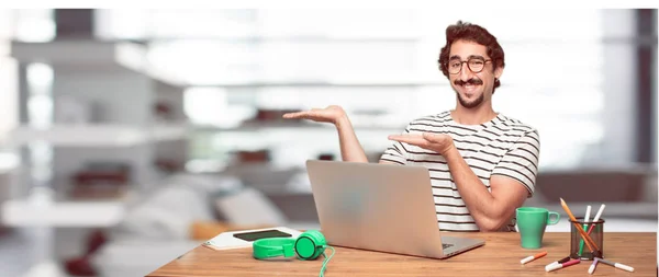 young bearded designer smiling with a satisfied expression showing an object or concept with one hand and with the other hand on the hip.