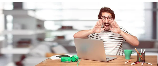 young bearded designer shouting loud like crazy, calling with hand with an angry expression, communicating a big announcement. Lateral or side view.