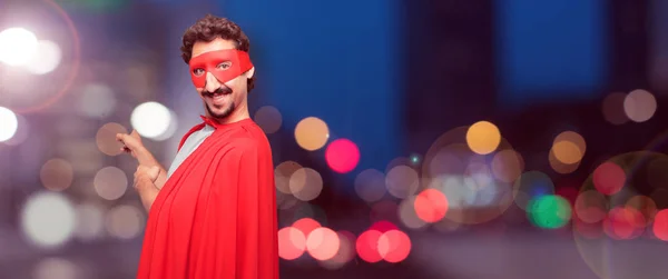 crazy man as a super hero smiling and pointing upwards with both hands, towards the place where the publicist may show a concept.