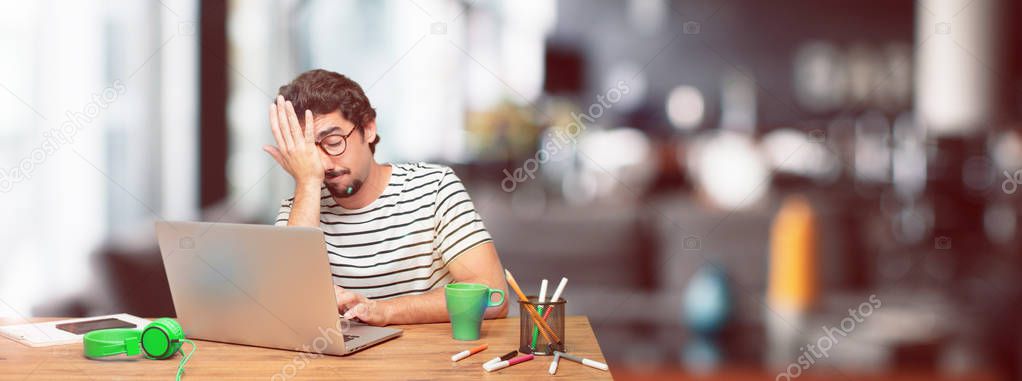 young bearded graphic designer with a laptop looking unenthusiastic and bored, listening to something dull and tedious and feeling like bearing a drag.