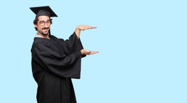 young graduated man smiling with a satisfied expression showing an object or concept which is held between both hands, laterally. clipart