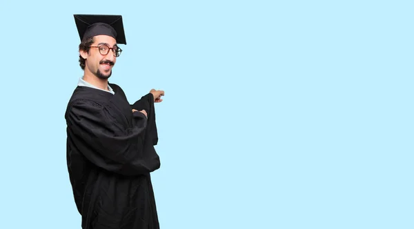 young graduated man smiling and pointing upwards with both hands, towards the place where the publicist may show a concept.