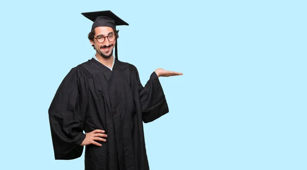 Junger Mann Mit Hochschulabschluss Lächelt Mit Zufriedenem Gesichtsausdruck Und Zeigt — Stockfoto