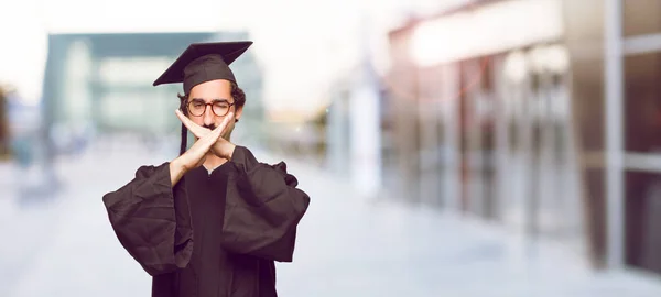 young graduated man with both hands crossed in front of mouth, in order to remain silent and keep a secret.