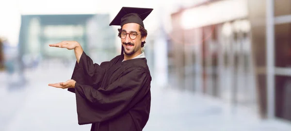 Jeune Homme Diplômé Souriant Avec Une Expression Satisfaite Montrant Objet — Photo