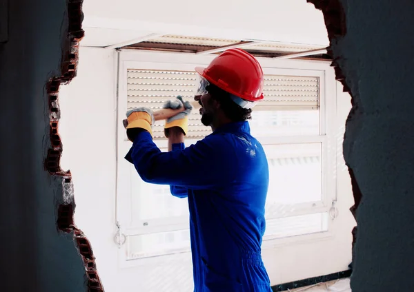 Young worker with a red protection helmet and wearing a blue boiler suit. Demolition concept.