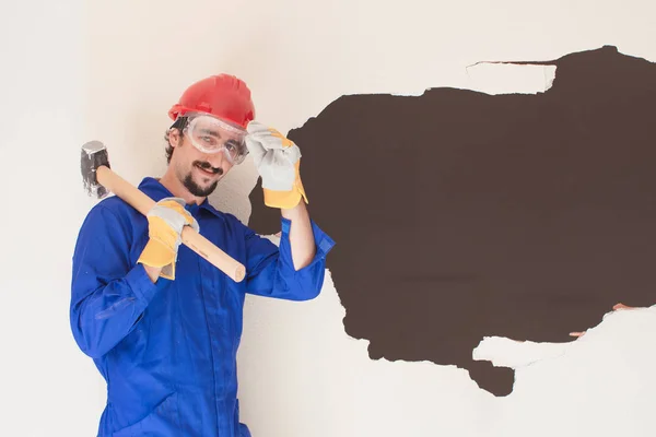 Young worker with a red protection helmet and wearing a blue boiler suit. Demolition concept.