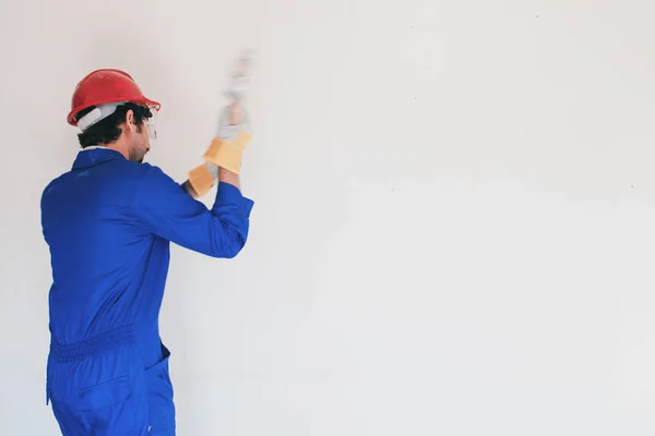 Young worker with a red protection helmet and wearing a blue boiler suit. Demolition concept.