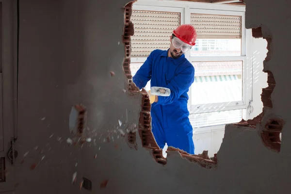 Young worker with a red protection helmet and wearing a blue boiler suit. Demolition concept.