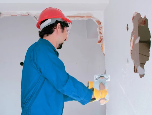 Young worker with a red protection helmet and wearing a blue boiler suit. Demolition concept.