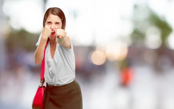 young pretty woman with an angry, aggressive and menacing pose, ready for the fight, showing fists furiously and belligerently.