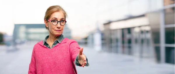 Beautiful adult blonde woman with a serious, confident, proud and stern expression offering a handshake, closing a deal, or greeting and welcoming you.