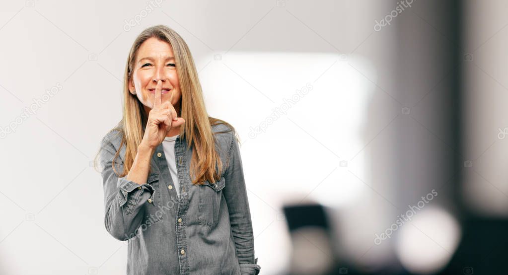 senior beautiful woman smiling, with index finger in front of mouth, requesting silence or sharing a secret