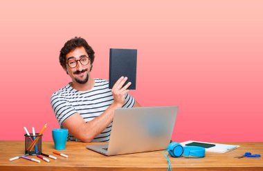 bir kitap ile bir dizüstü bilgisayar ile bir masa üzerine çılgın genç grafik tasarımcı