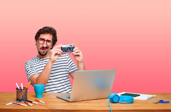 young crazy graphic designer on a desk with a laptop and with a vintage camera