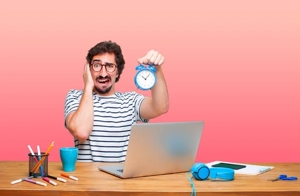 young crazy graphic designer on a desk with a laptop and with an alarm clock