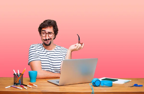 young crazy graphic designer on a desk with a laptop and with a smoke vintage pipe