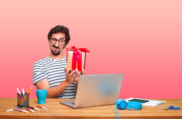 young crazy graphic designer on a desk with a laptop and with gift box concept