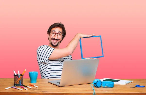 young crazy graphic designer on a desk with a laptop and with a frame