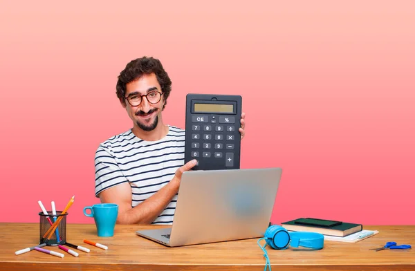 young crazy graphic designer on a desk with a laptop and with a calculator
