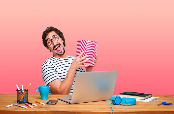 young crazy graphic designer on a desk with a laptop and with a pop corn bucket