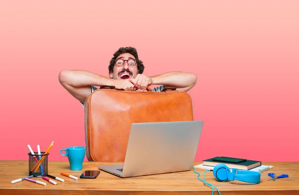 young crazy graphic designer on a desk with a laptop and with a leather case luggage