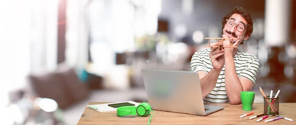 young crazy graphic designer on a desk with a laptop and with a wooden plane