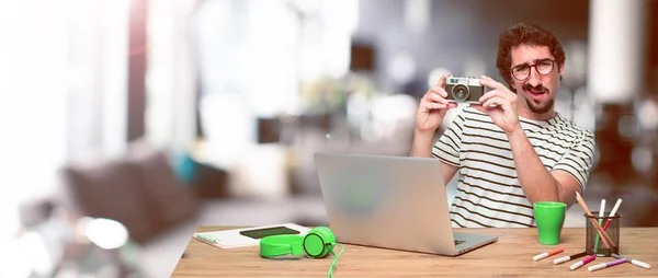 young crazy graphic designer on a desk with a laptop and with a vintage camera