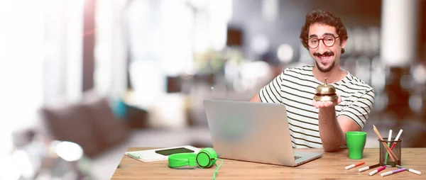 young crazy graphic designer on a desk with a laptop and with a ring bell