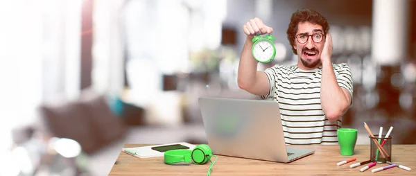 young crazy graphic designer on a desk with a laptop and with an alarm clock