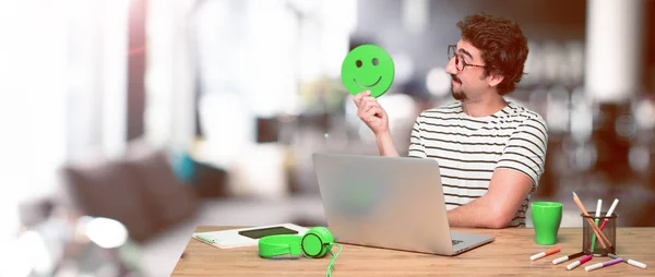 young crazy graphic designer on a desk with a laptop and with a smiley emoticon