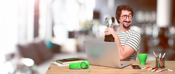 young crazy graphic designer on a desk with a laptop and holding a trophy