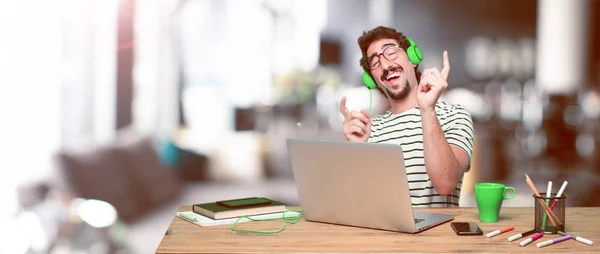 young crazy graphic designer on a desk with a laptop and listening music with a headphones