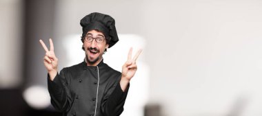 Genç adam şef gurur, mutlu ve kendine güvenen bir ifade ile; gülümseyen ve göstermek uzakta başarı ise her iki el ile el zafer zafer kutluyor bir 