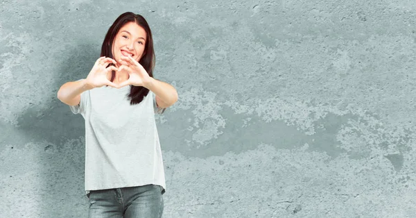 young pretty girl full body standing sideways, smiling, looking happy and in love, making the shape of a heart with hands. Side or lateral view.