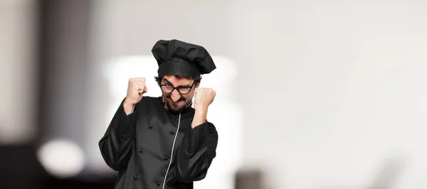 young man chef with an angry, aggressive and menacing pose, ready for the fight, showing fists furiously and belligerently.