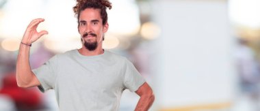 tek eliyle tutan bir küçük bir nesne veya kavramı, gösterilen memnun bir ifadeyle gülümseyen genç hipster adam.